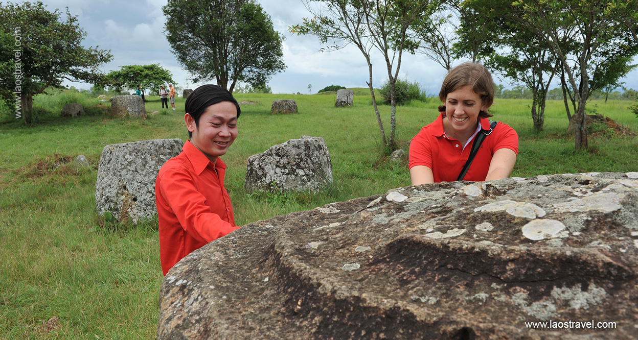 A Laos Travel tour guide and an American tourist smiling at the camera in front of a large stone jar