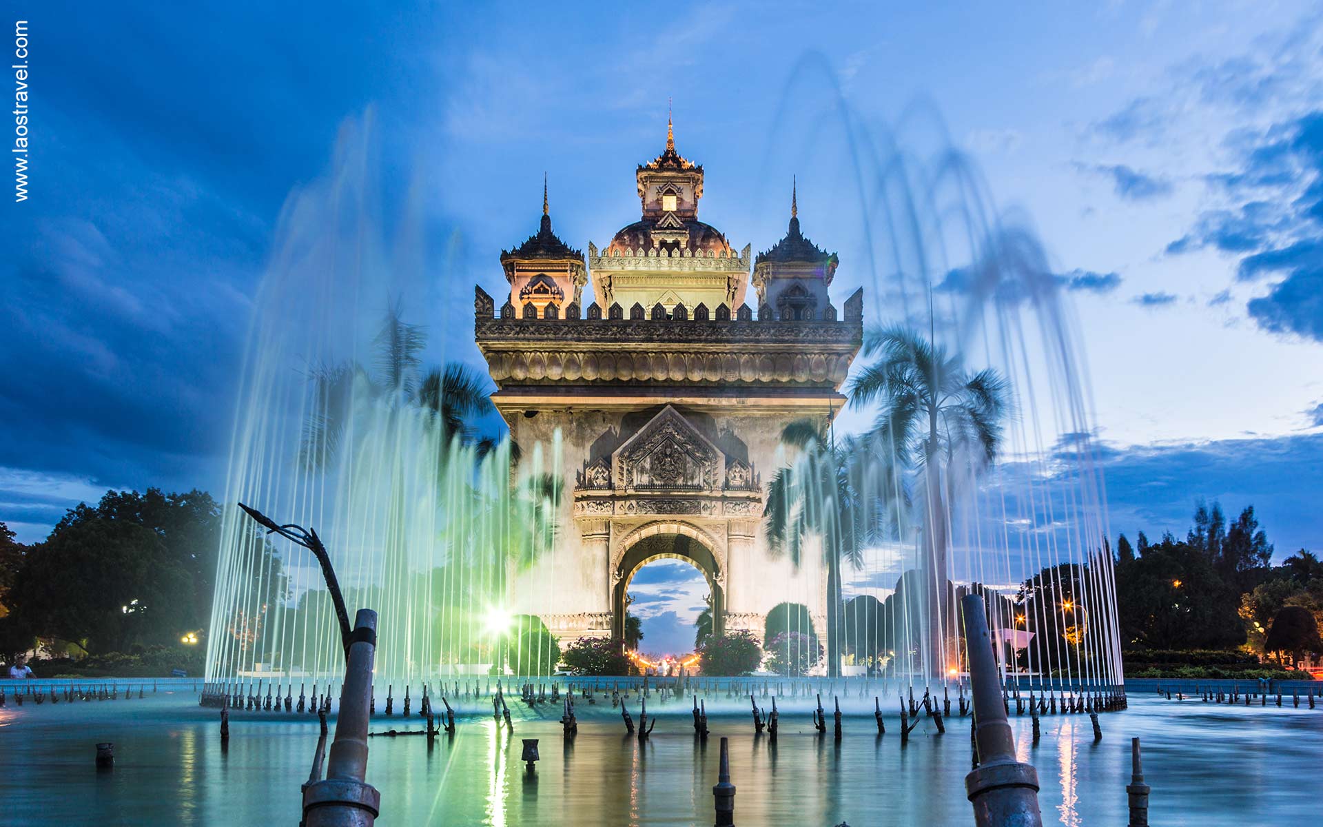 A stunning shot of Patuxai lit up by fountains and the setting sun